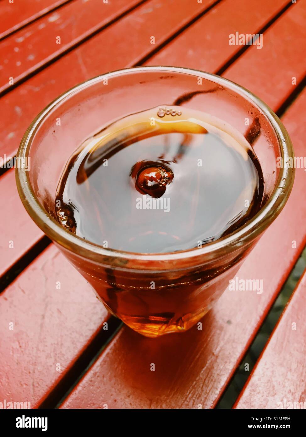 Ein Glas schwarzen Tee auf einem roten hölzernen Tisch Stockfoto
