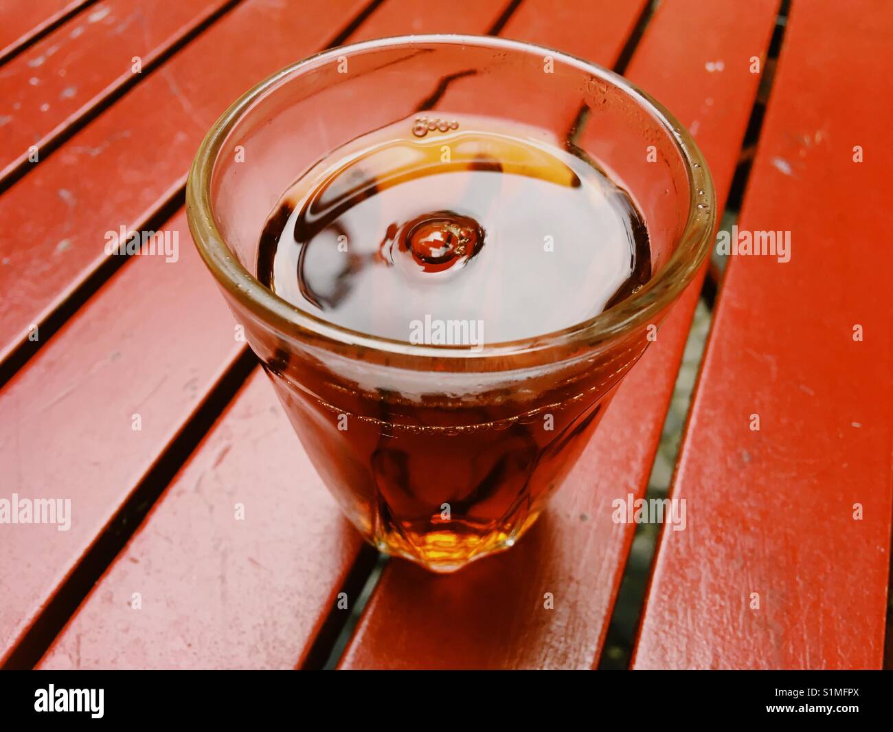 Ein Glas schwarzen Tee auf einem roten hölzernen Tisch Stockfoto