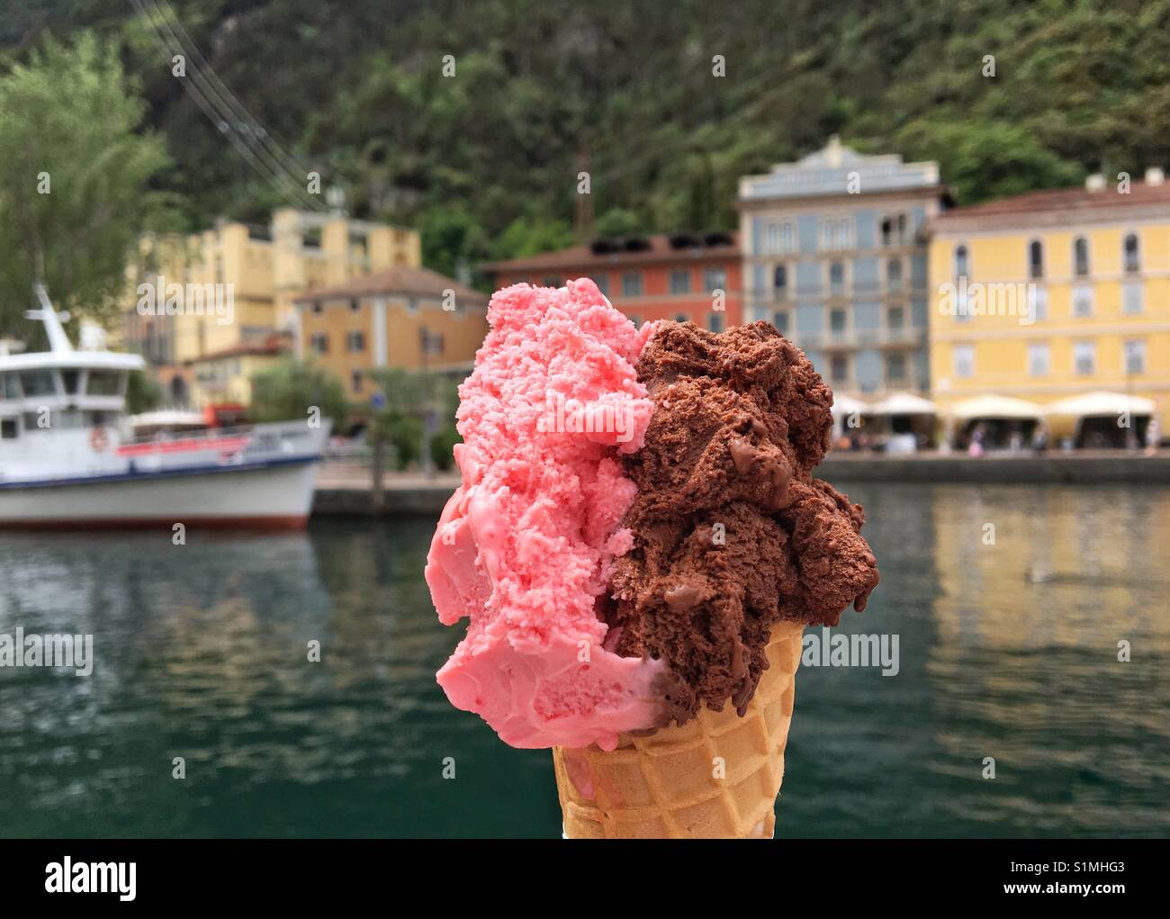 Italienisches Eis "Gelato" mit dem Hafen von Riva del Garda im Hintergrund Stockfoto