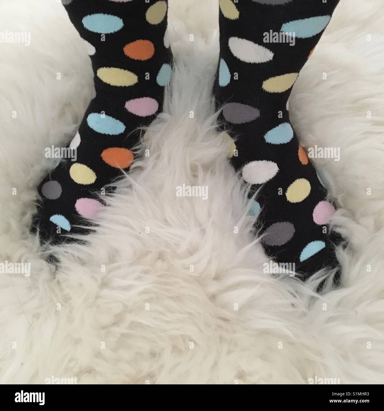 Füße in Polka Dot Socken auf Flauschigen Schaffell Teppich Stockfoto