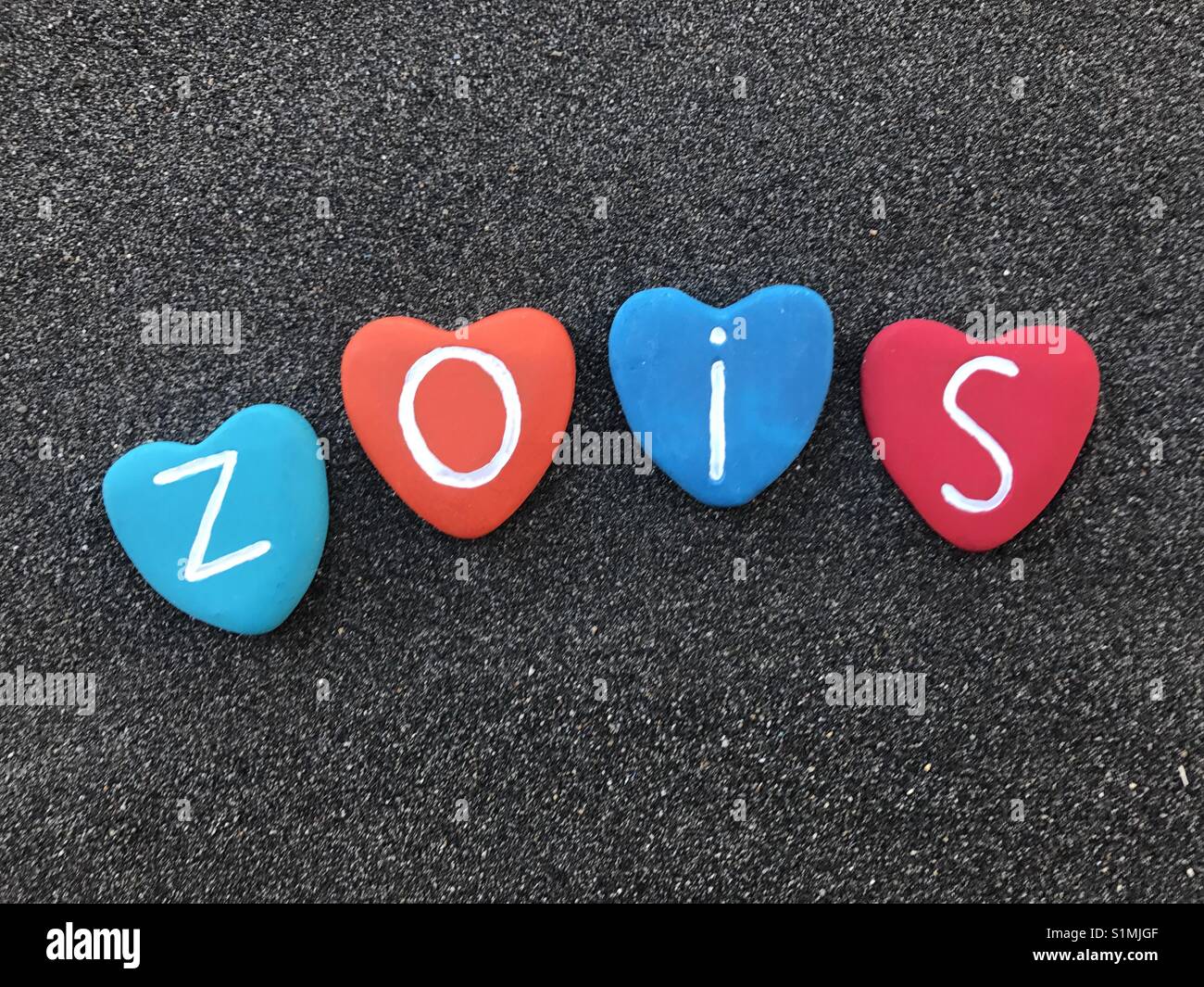 Zois, griechischer Herkunft männliche Namen mit bunten Herzen Steine über schwarzen vulkanischen Sand Stockfoto