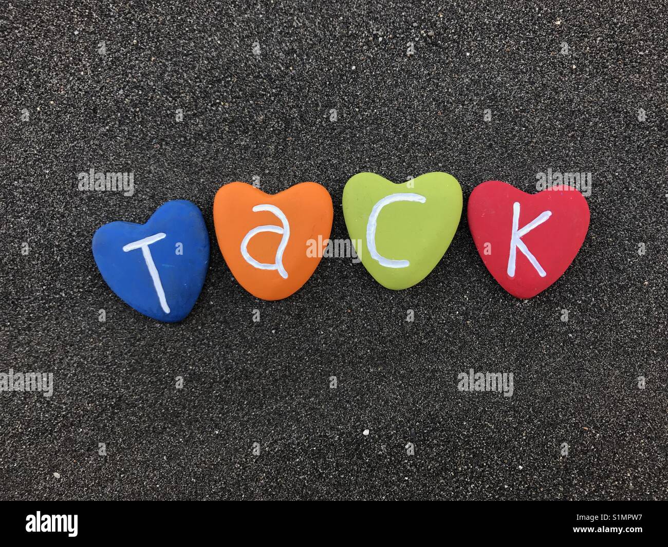 Tack Wort mit bunten Herzen Steine über schwarzen vulkanischen Sand Stockfoto