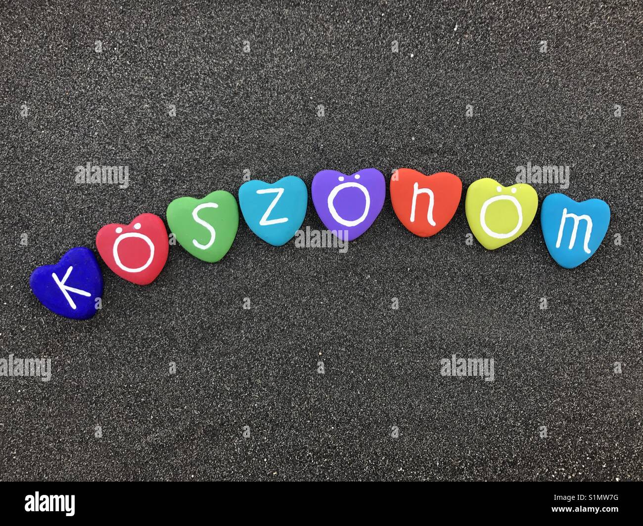 Köszönöm, ungarisch Danke mit bunten Herzen Steine über schwarzen vulkanischen Sand - Smartphone-aufgenommenes Stockfoto