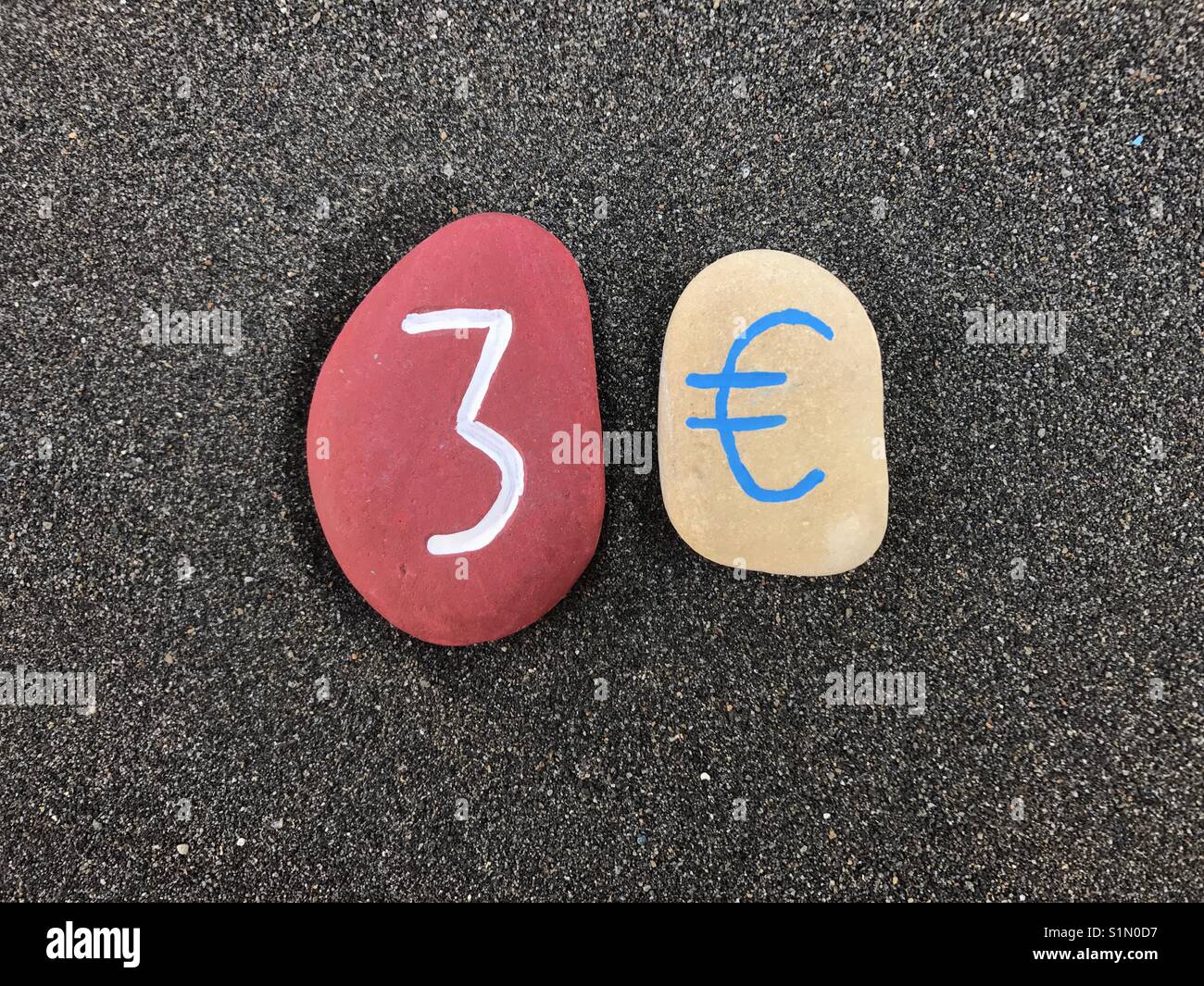 3 Euro mit farbigen Steinen über schwarzen vulkanischen Sand - Smartphone-aufgenommenes Stockfoto
