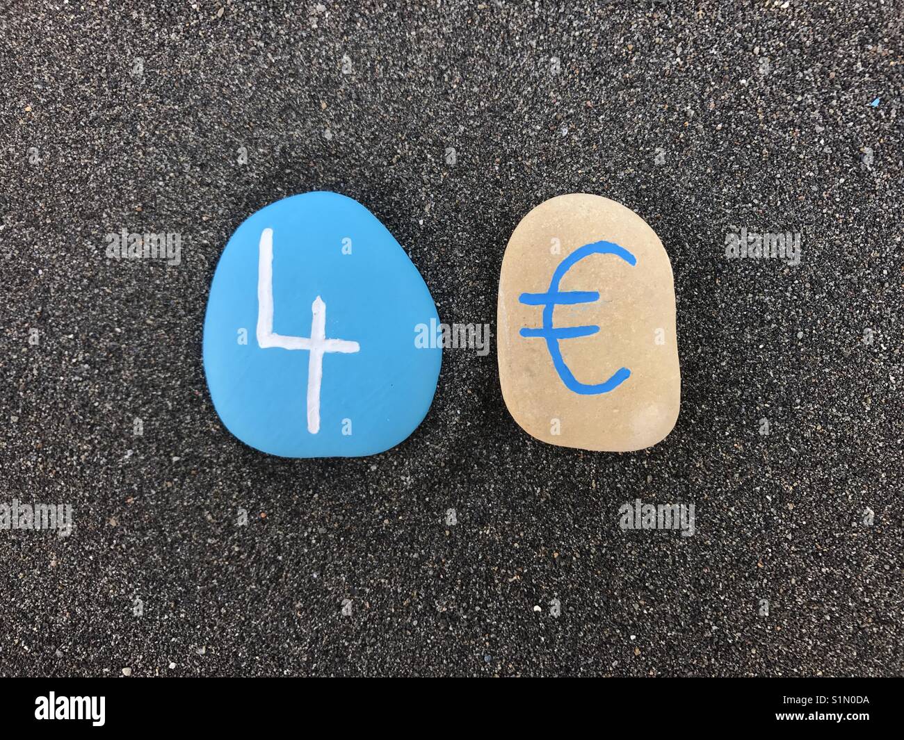 4 Euro mit farbigen Steinen über schwarzen vulkanischen Sand - Smartphone-aufgenommenes Stockfoto