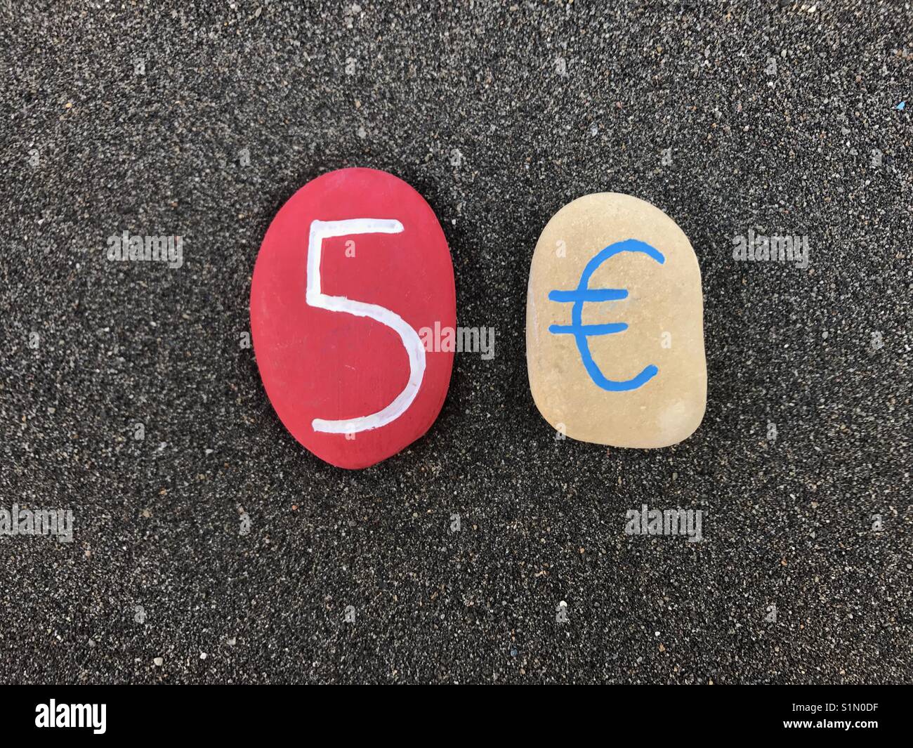5 Euro mit farbigen Steinen über schwarzen vulkanischen Sand - Smartphone-aufgenommenes Stockfoto