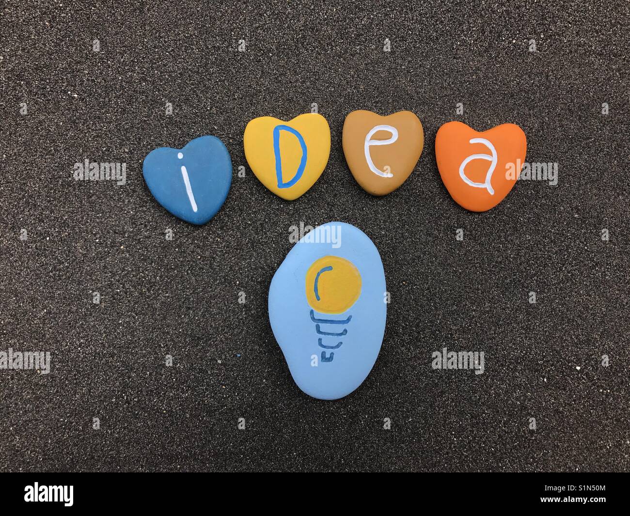 Idee und Lampe Design mit farbigen Steinen über schwarzen vulkanischen Sand - Smartphone-aufgenommenes Stockfoto