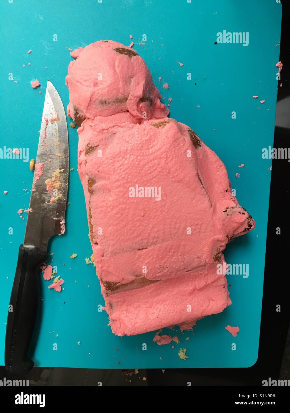 Lego mann Kuchen mit seinem Arm abschneiden und ein Messer neben ihm - Smartphone-aufgenommenes Stockfoto