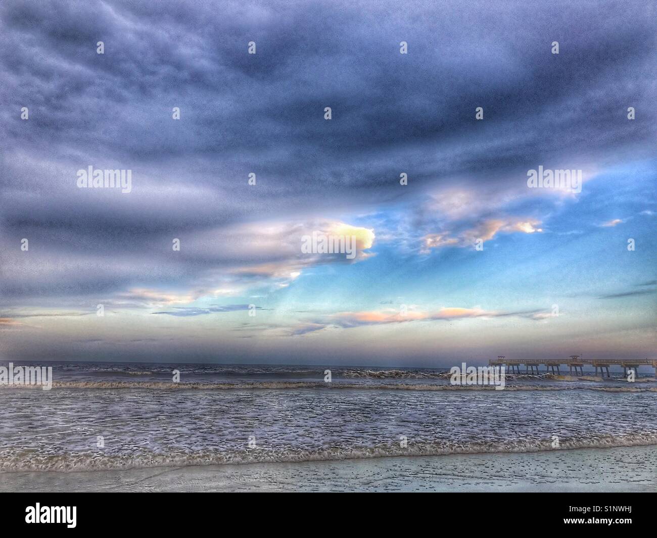 Dramatische Wolken Rolle bei Sonnenuntergang über dem Ozean, verlassenen Pier auf der rechten Horizont Stockfoto