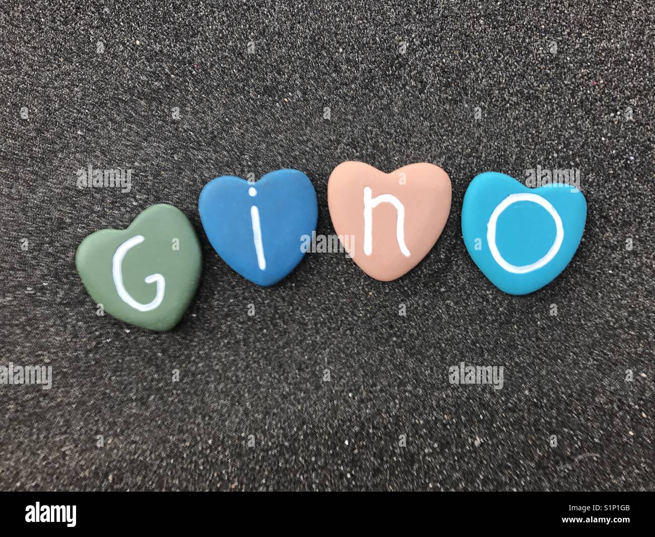 Gino, männliche italienischen Namen mit bunten Herzen Steine über schwarzen vulkanischen Sand Stockfoto