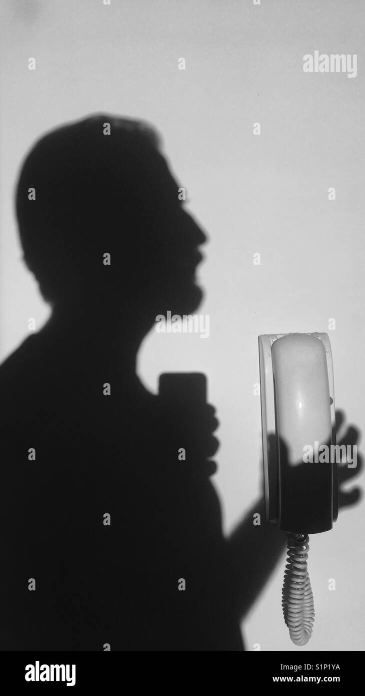 Schatten von einem Mann mit einem an der Wand befestigten Telefon Headset Stockfoto