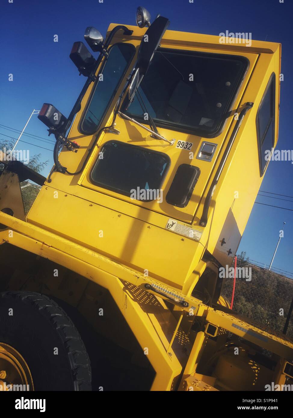Gelbe schwere Ausrüstung an einem Flughafen vor blauem Himmel - Smartphone-aufgenommenes Stockfoto