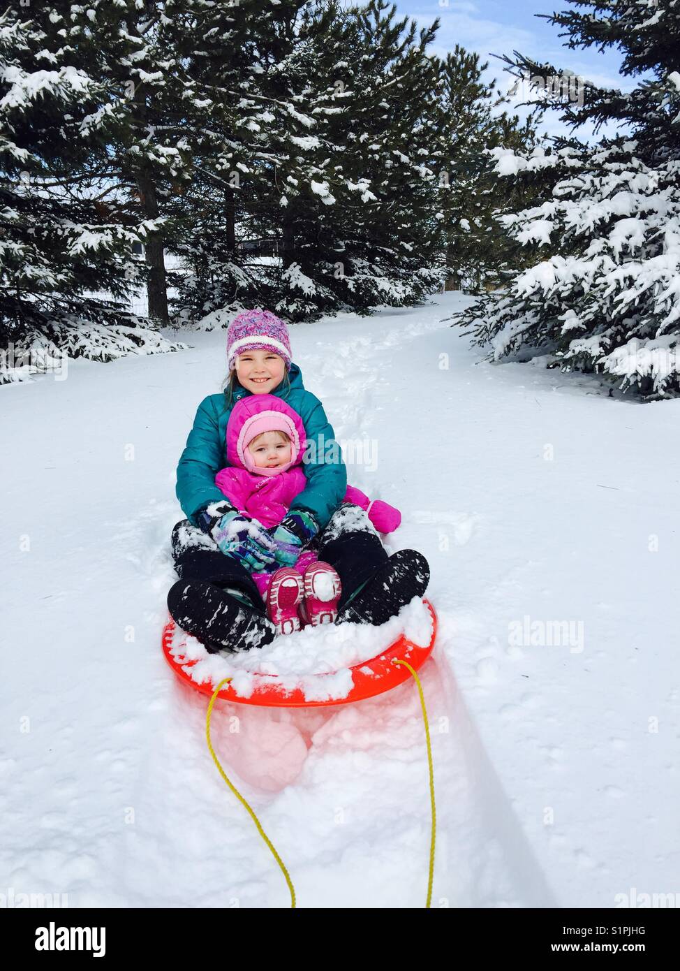 Junge Mädchen und Baby auf Plastikschlitten im Winterschnee. Stockfoto