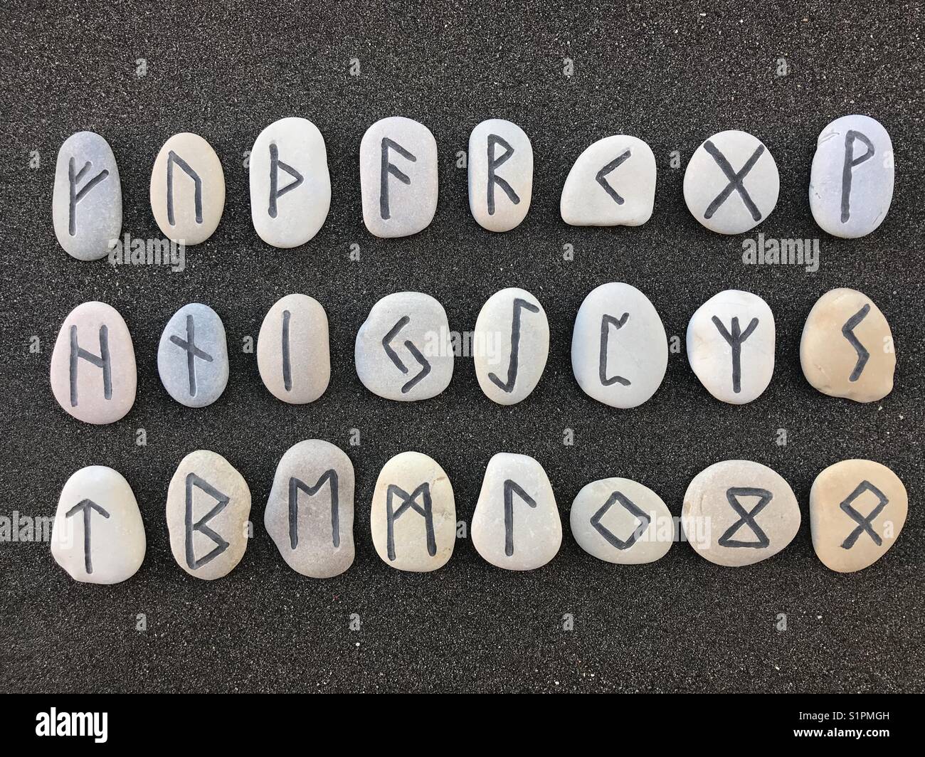 Runisches Alphabet oder Futhark nach den ersten sechs Buchstaben mit geschnitzten Steinen auf schwarzem vulkanischem Sand Stockfoto