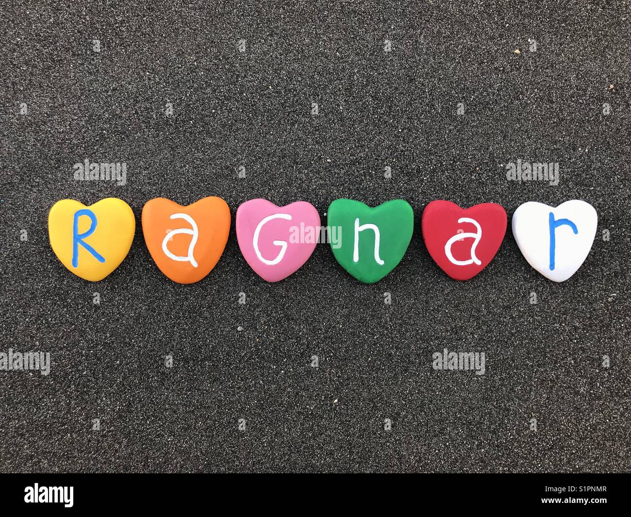Ragnar, skandinavischen männliche Name und Altnordischen Ursprung zusammen mit bunten Herzen Steine über schwarzen vulkanischen Sand Stockfoto