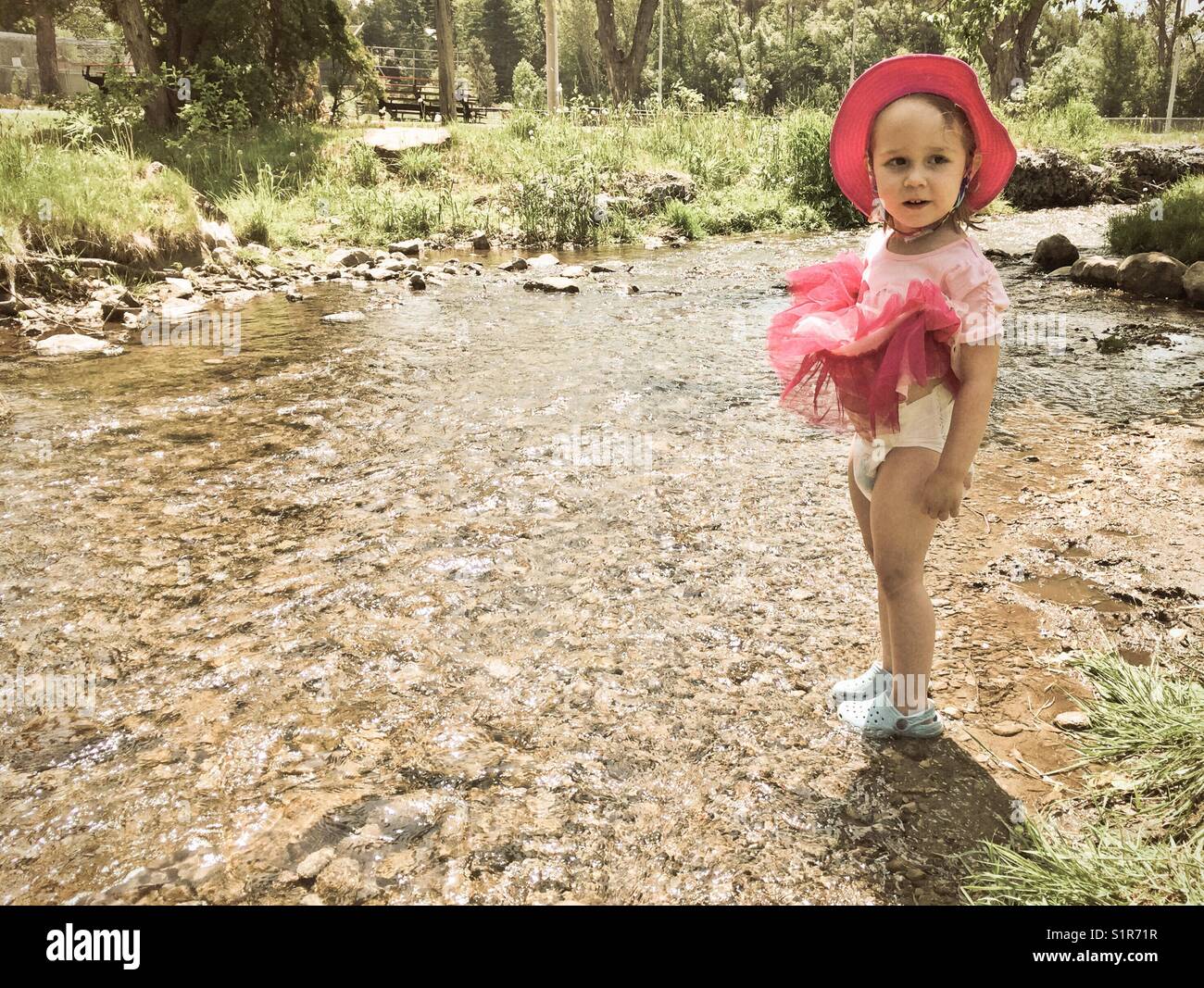 Nostalgisches Foto von Toddler stehendes Mädchen im Stream. Ziehen Sie ihr Kleid zeigt ihre Windel Stockfoto
