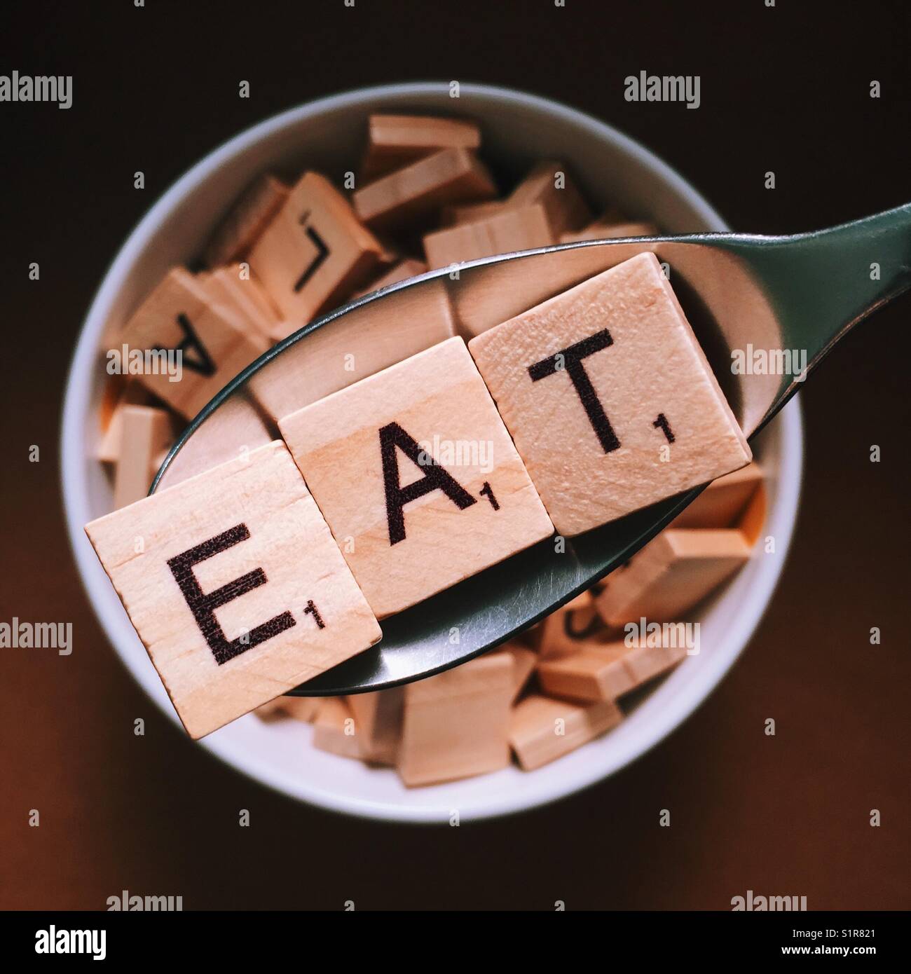Nahaufnahme eines Löffels Essen mit Holzbuchstaben auf Rechtschreibung und eine Schüssel voller Holzbuchstaben darunter Stockfoto