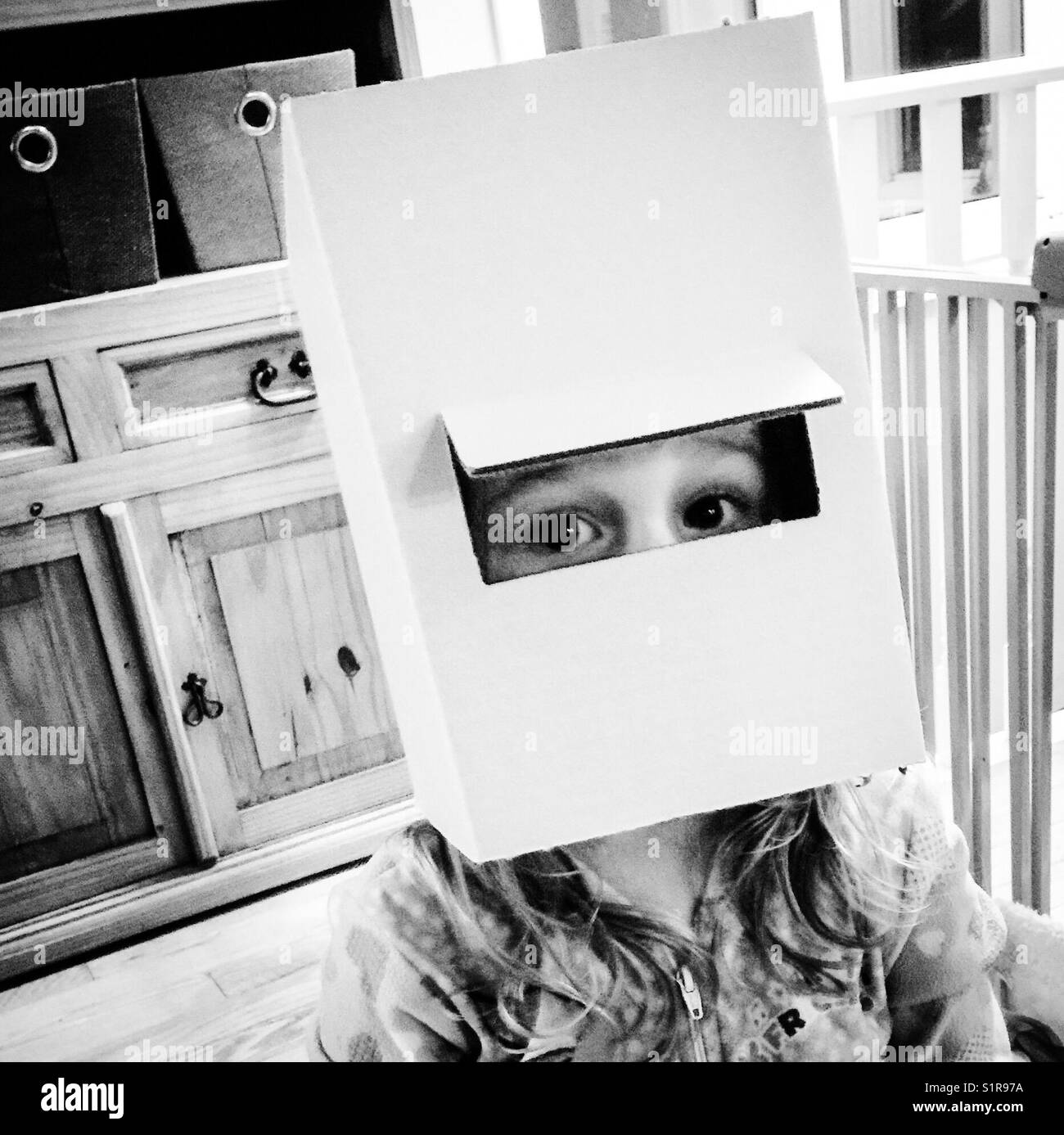 Junges Mädchen mit einem Pappkarton auf dem Kopf und spähen durch einen Ausschnitt Bohrung Stockfoto