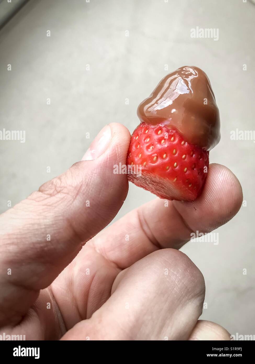 Die Hand hält eine Erdbeere mit Karamell - Smartphone-aufgenommenes Stockfoto