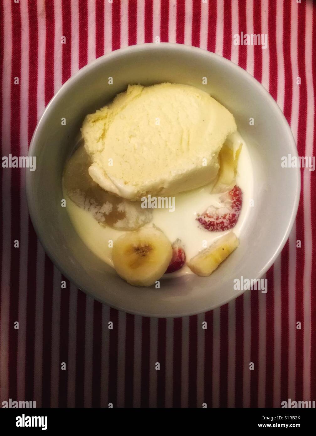 Eine Schüssel mit Obst und Eis, die in Doppelcreme schweben. Auf einem gestreiften Tischtuch sitzen. - Smartphone-aufgenommenes Stockfoto