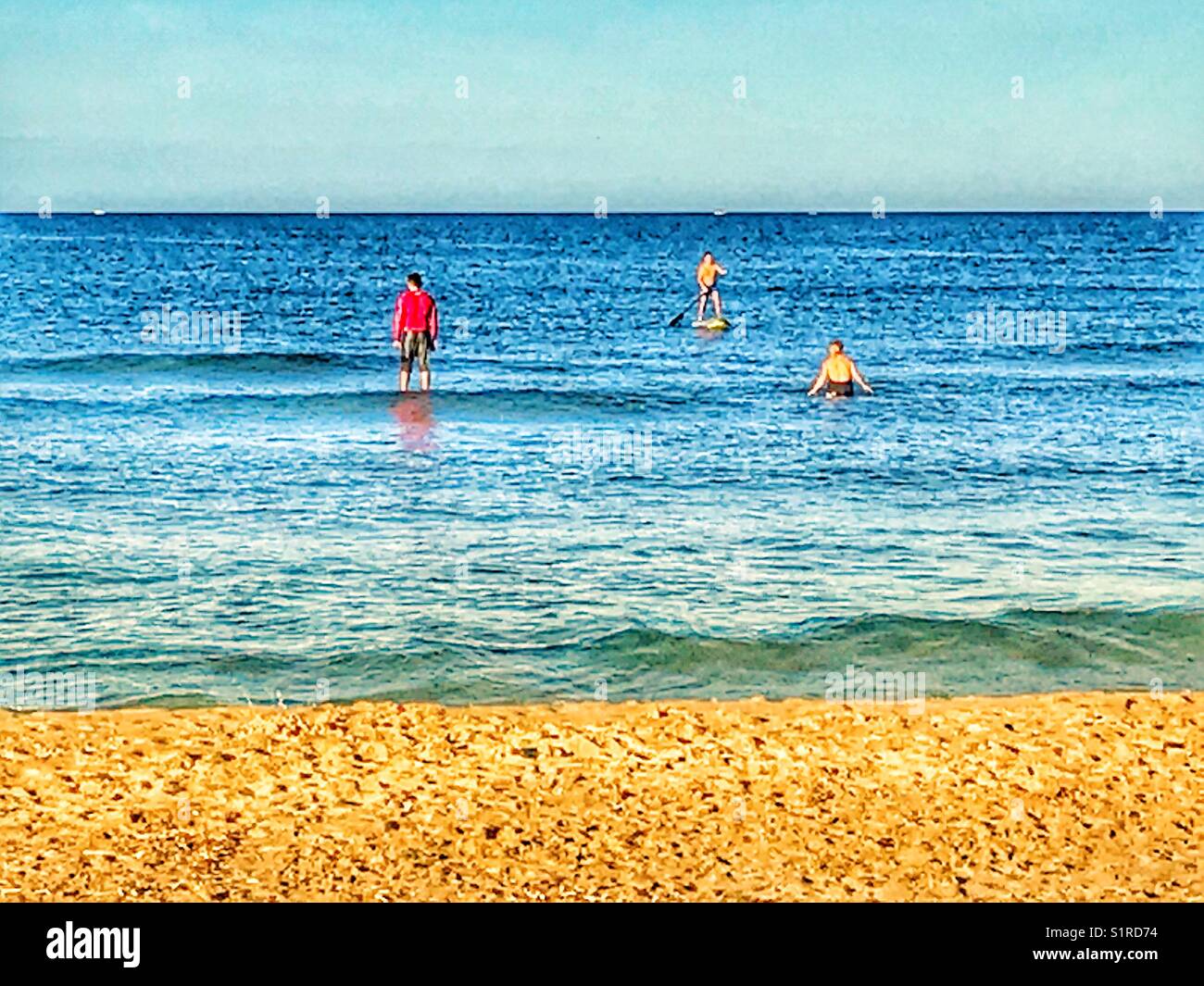 Drei Menschen im Meer, einschließlich zwei auf Paddle Boards. Arenal Strand, Javea, Alicante, Spanien. Stockfoto
