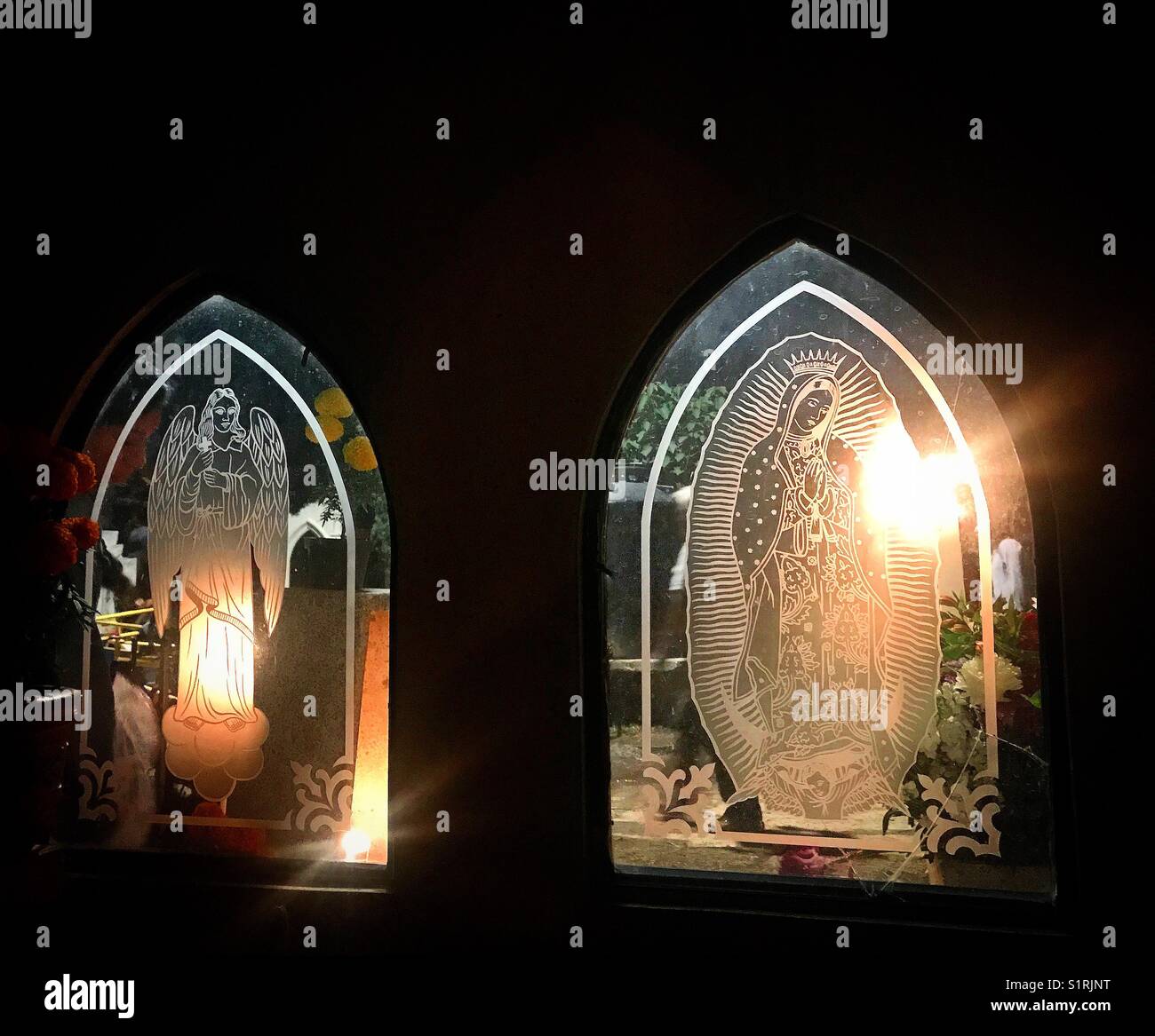 Windows mit dem Bild eines Engels und Unserer Lieben Frau von Guadalupe, die von Kerzen auf dem Friedhof leuchtet während Tag der Toten in San Gregorio Atlapulco, Xochimilco, Mexiko Stadt. - Smartphone-aufgenommenes Stockfoto