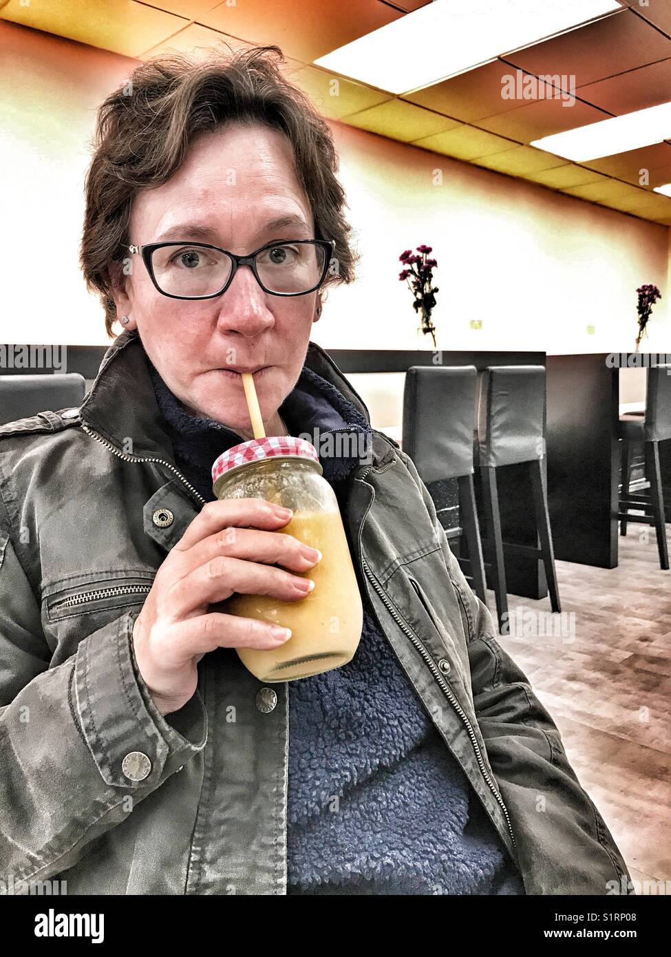 Frau trinkt ein Fruit Smoothie aus Glas mit Strohhalm, in einer italienischen Eisdiele, Ecco Gelato, Sherbourne, Dorset, England - Smartphone-aufgenommenes Stockfoto