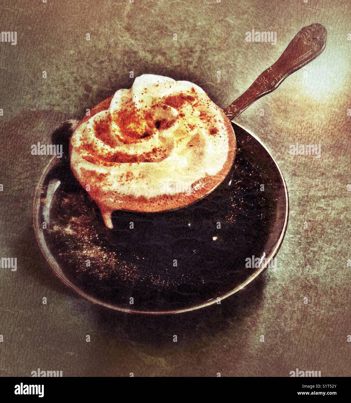 Heiße Schokolade mit Schlagsahne und Zimt in einer kleinen schwarzen Tasse und Untertasse mit Löffel - Smartphone-aufgenommenes Stockfoto