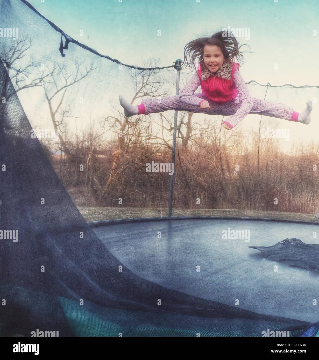 Mädchen, das Splits in der Luft auf einem alten Trampolin macht Stockfoto