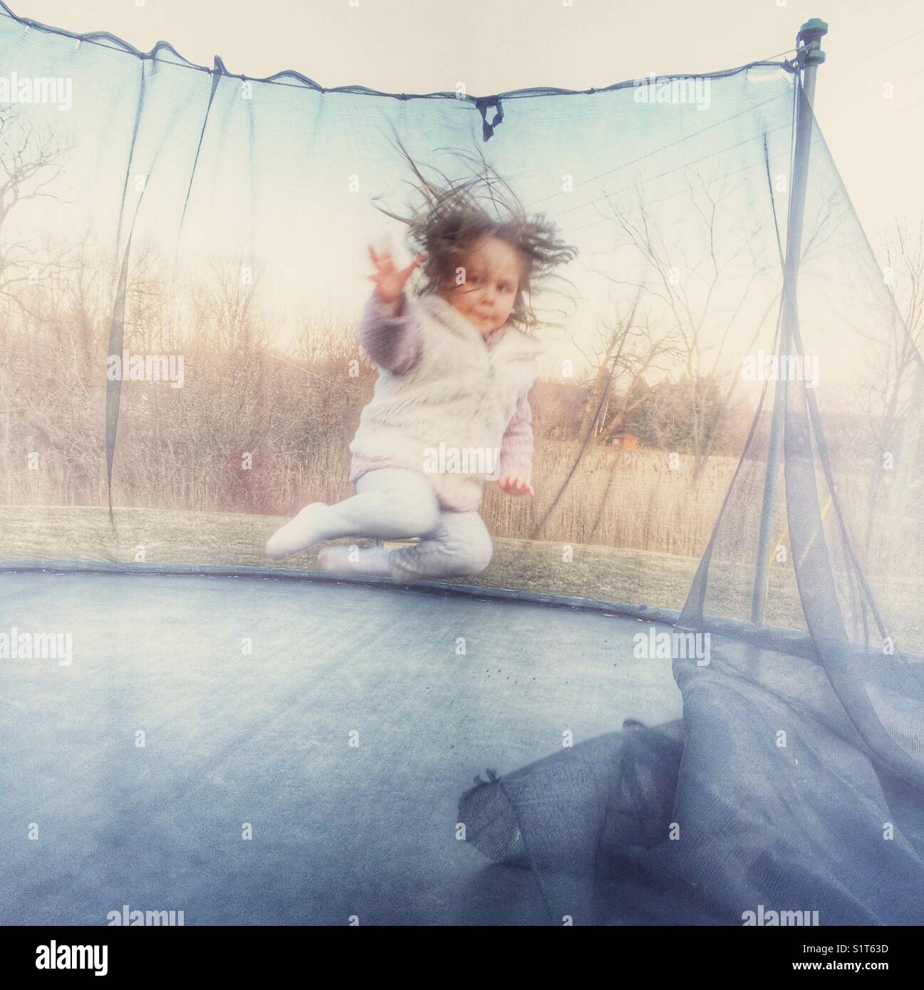 Kleinkind Mädchen mitten in der Luft gefangen, während auf einem alten heruntergekommenen Trampolin außerhalb springen Stockfoto