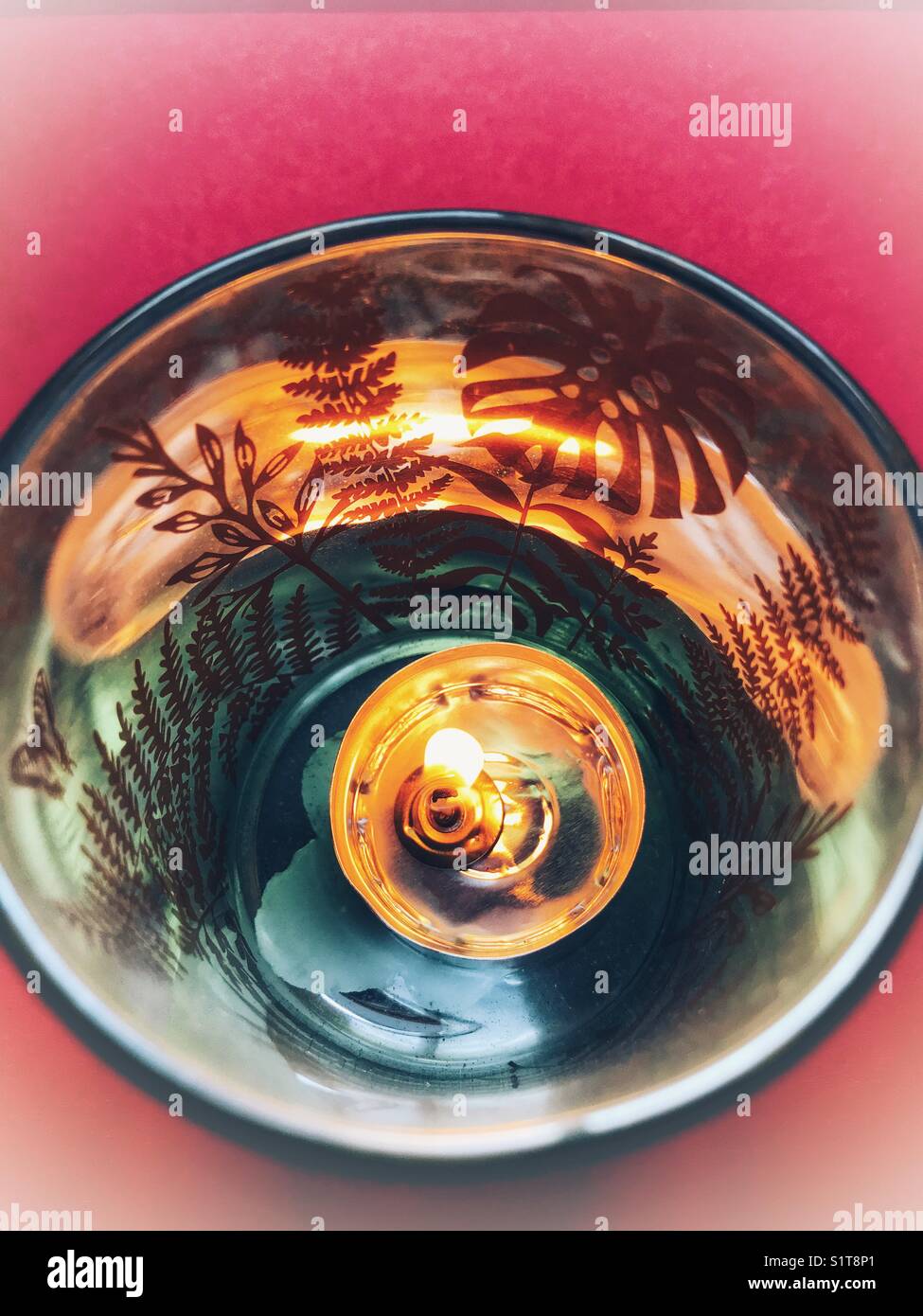 Teelicht Kerze brennt in einem Glaskerzenhalter auf rotem Hintergrund Stockfoto