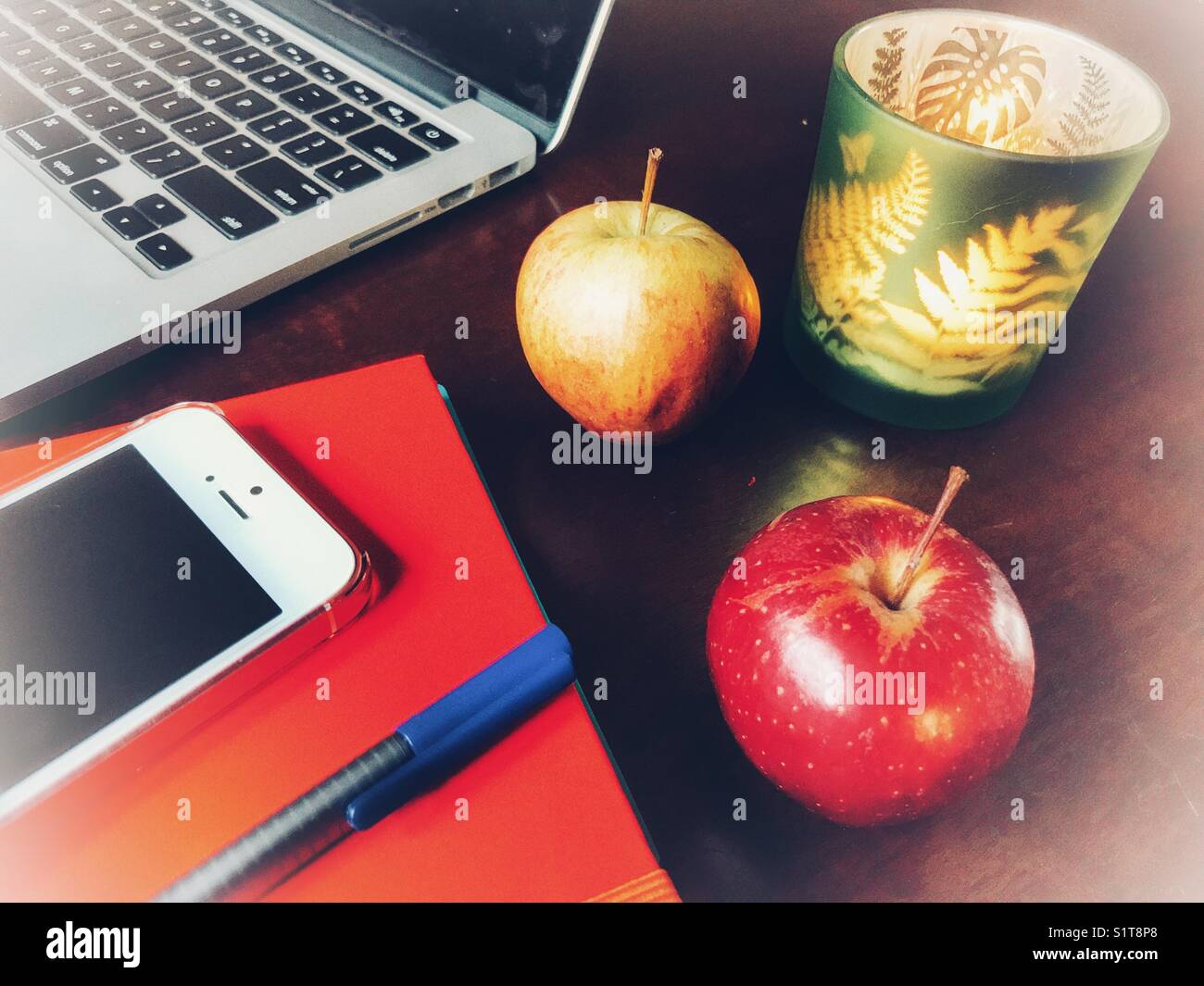 Desktop mit dem MacBook, Äpfel, Zeitschriften, iPhone, Stift und Kerze im Glas. Hohe Betrachtungswinkel - Smartphone-aufgenommenes Stockfoto