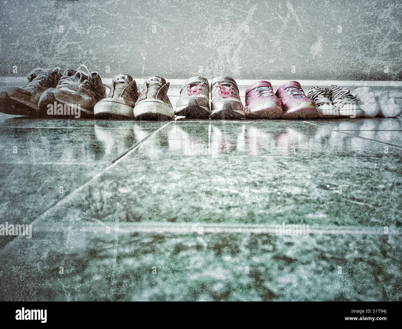 Familie Schuhe in einer Reihe auf einem gefliesten Boden gegen eine Wand. Stockfoto