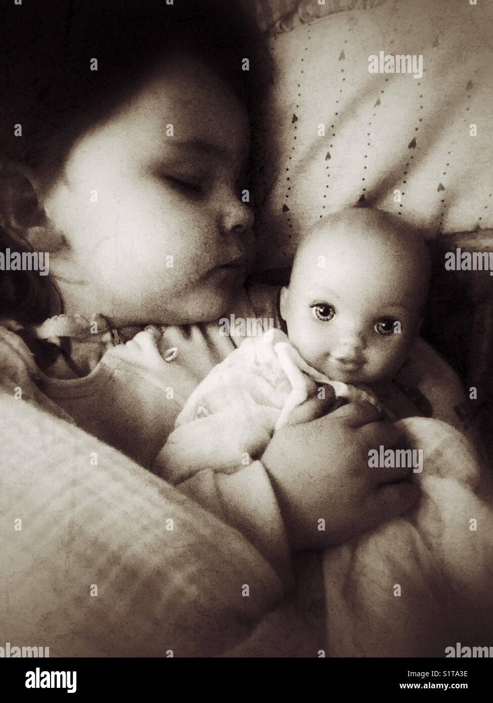Ein kleines Mädchen, das mit ihrer Babypuppe schläft - Smartphone-aufgenommenes Stockfoto Ein kleines Mädchen, das mit ihrer Babypuppe schläft - Smartphone-aufgenommenes Stockfoto