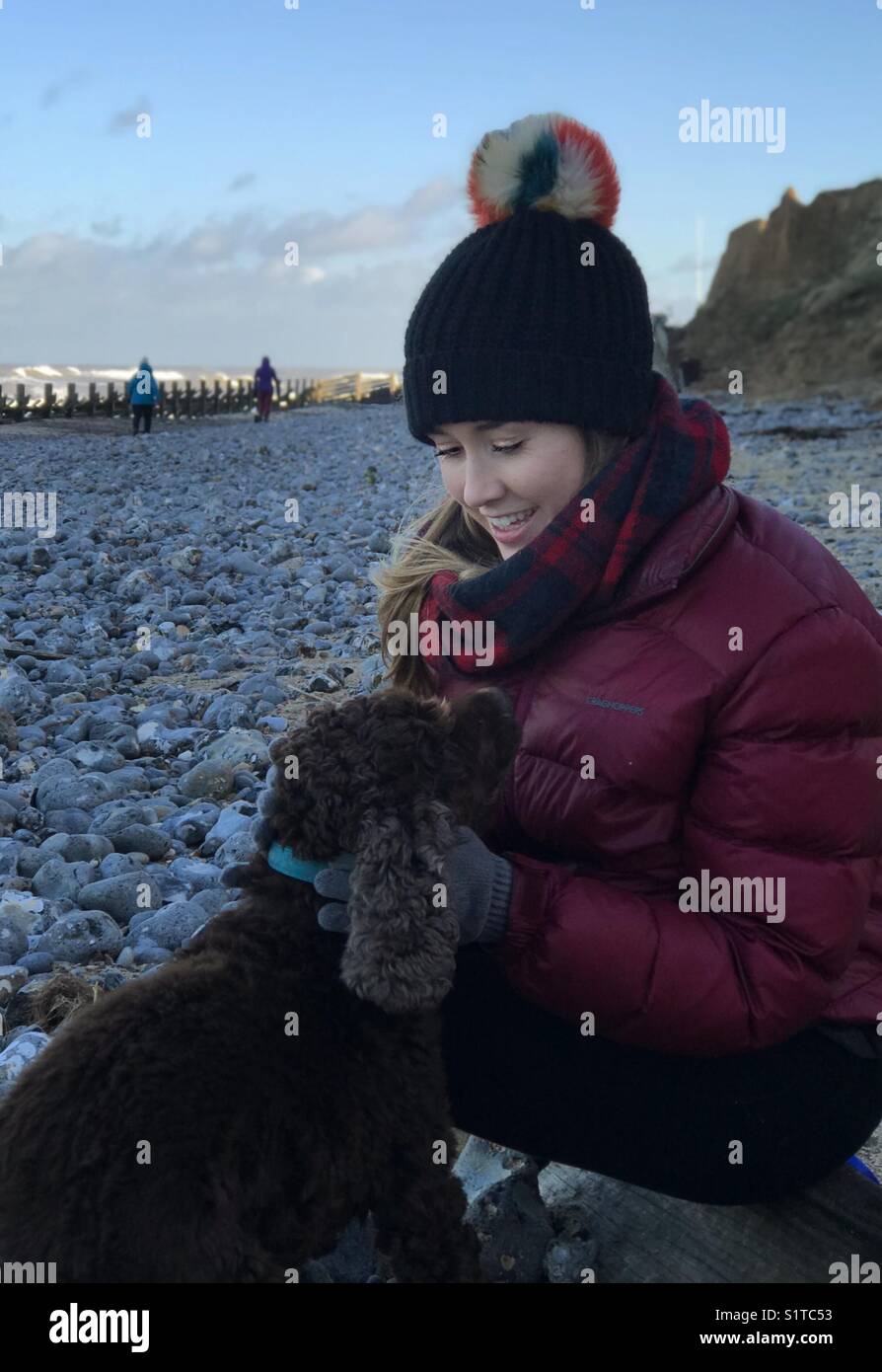 Junge Frau an einem Kiesstrand mit einem Cocker Spaniel im Winter - Smartphone-aufgenommenes Stockfoto