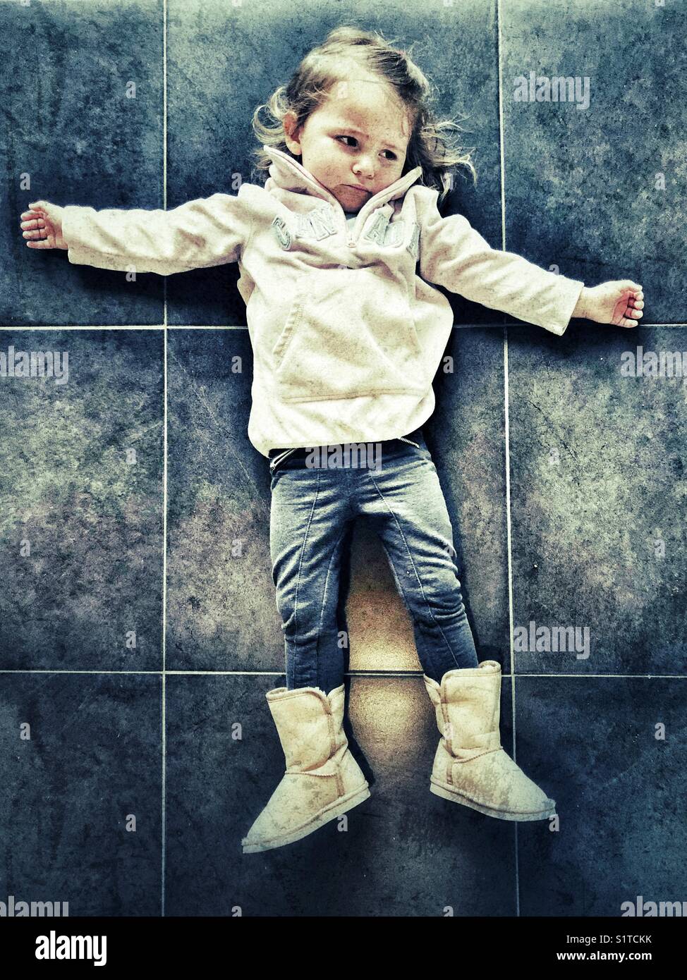 Mürriges Kleinkind, das sich auf Fliesenboden legt, kurz vor einem Wutanfall Stockfoto