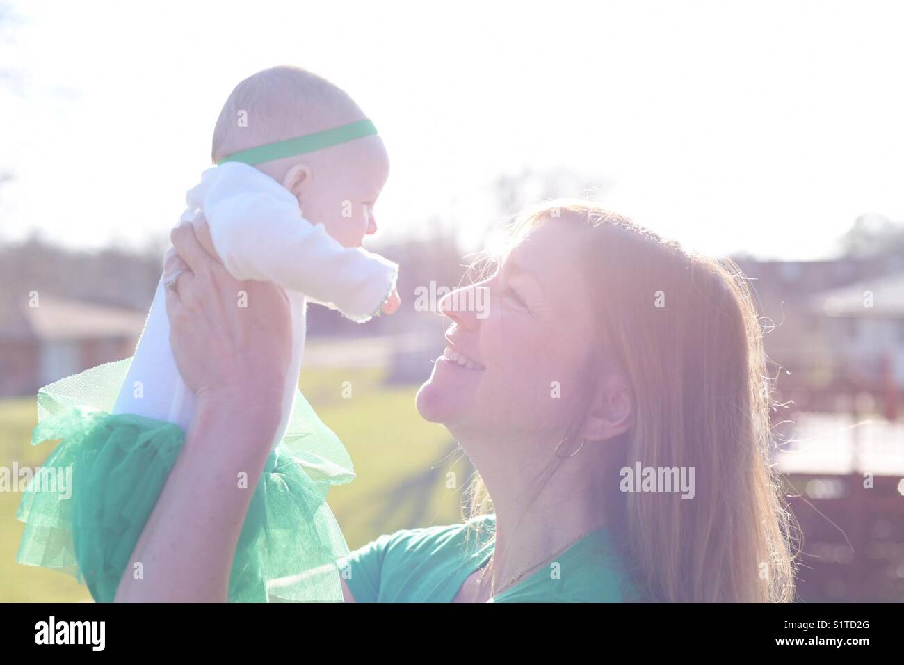 Woman Holding up baby draußen im hellen Sonnenlicht auf der St Patrick's Day Stockfoto