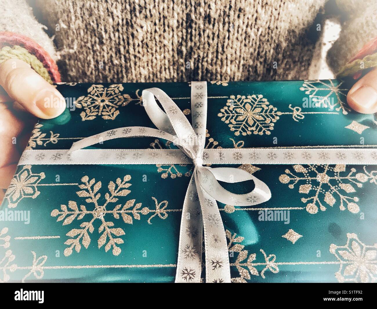 Frau, die ein Weihnachtsgeschenk in Blau mit weißem Band hält, Mittelteil, Nahaufnahme - Smartphone-aufgenommenes Stockfoto