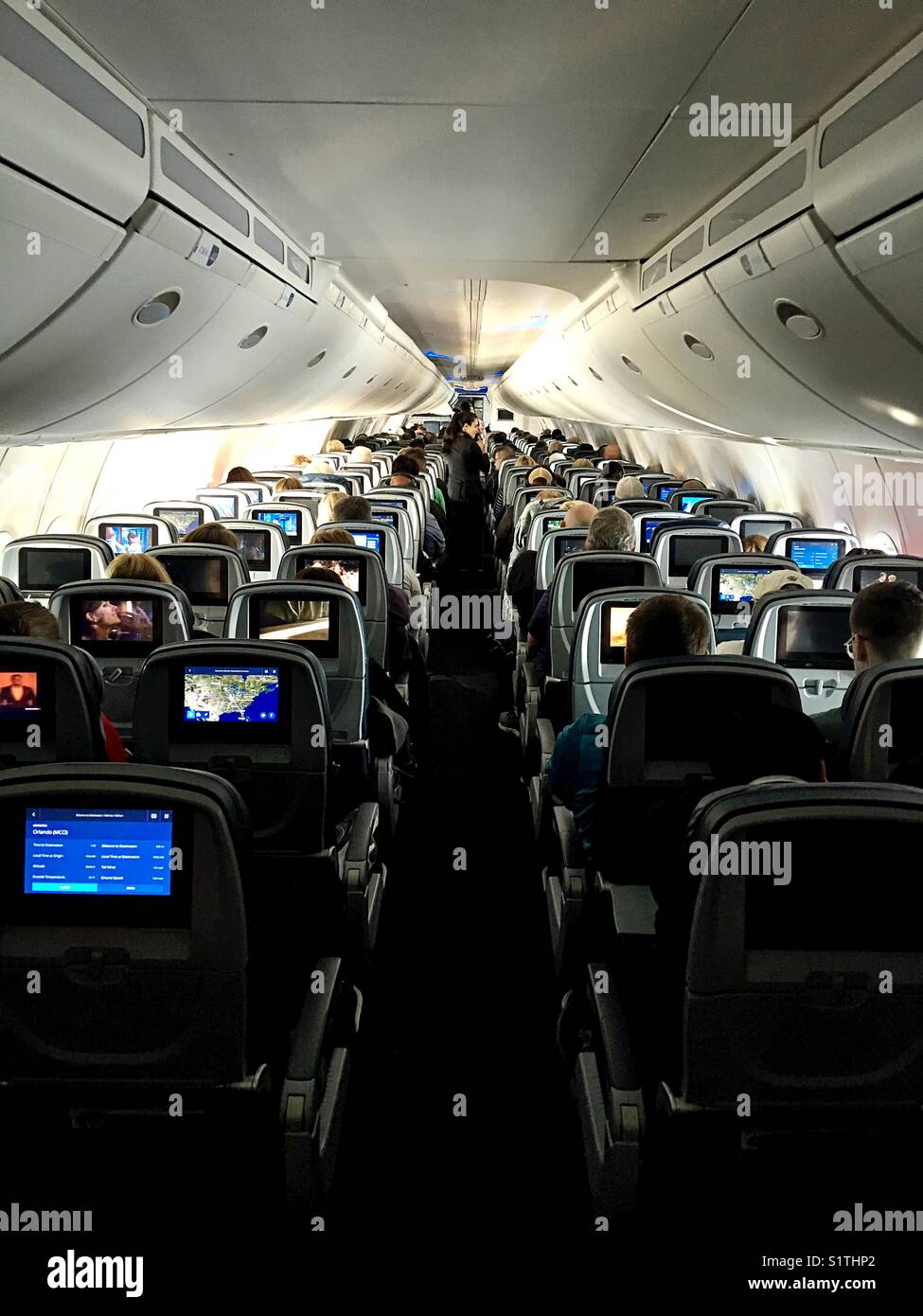 Die Kabine eines Flugzeugs mit Menschen Filme auf ihren Bildschirmen, wie von der Rückseite der Flugzeug gesehen. Stockfoto