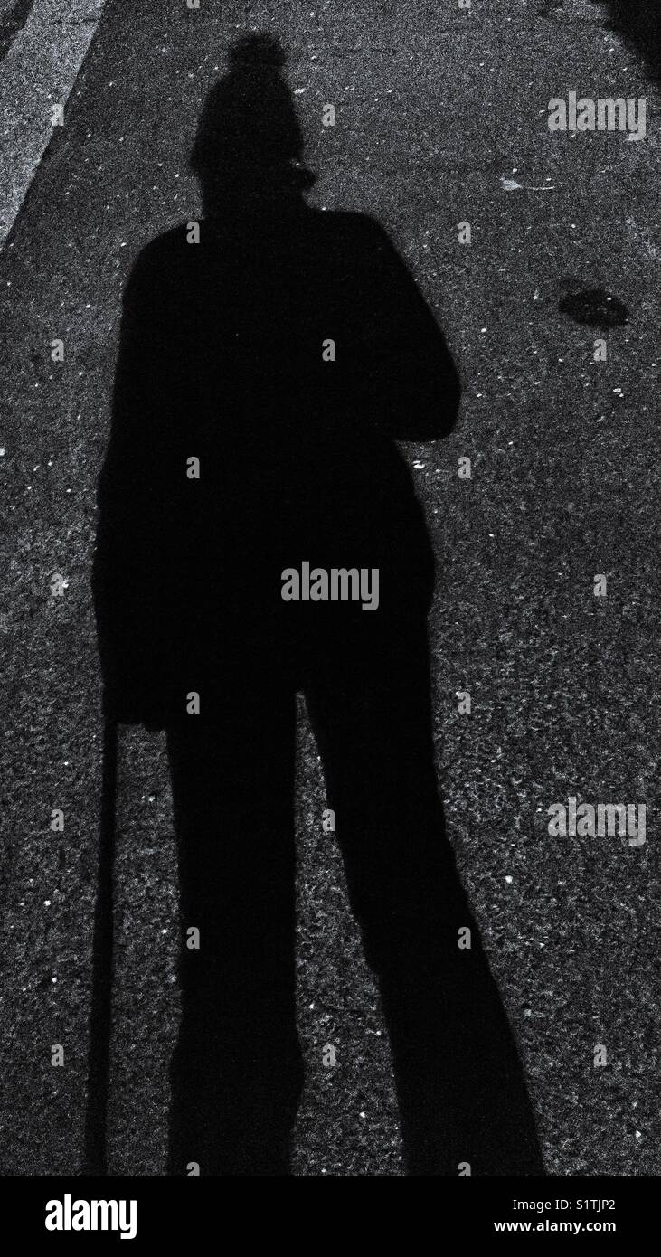 Silhouette einer Person in einem Wackelhut mit einem Wheelie-Koffer - Smartphone-aufgenommenes Stockfoto