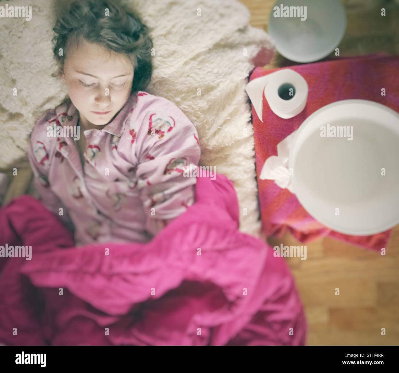 Mädchen krank mit Magen Virus schlafend auf dem Sofa in Decken mit kranken Schaufel und Klopapierrolle abgedeckt neben ihr Stockfoto