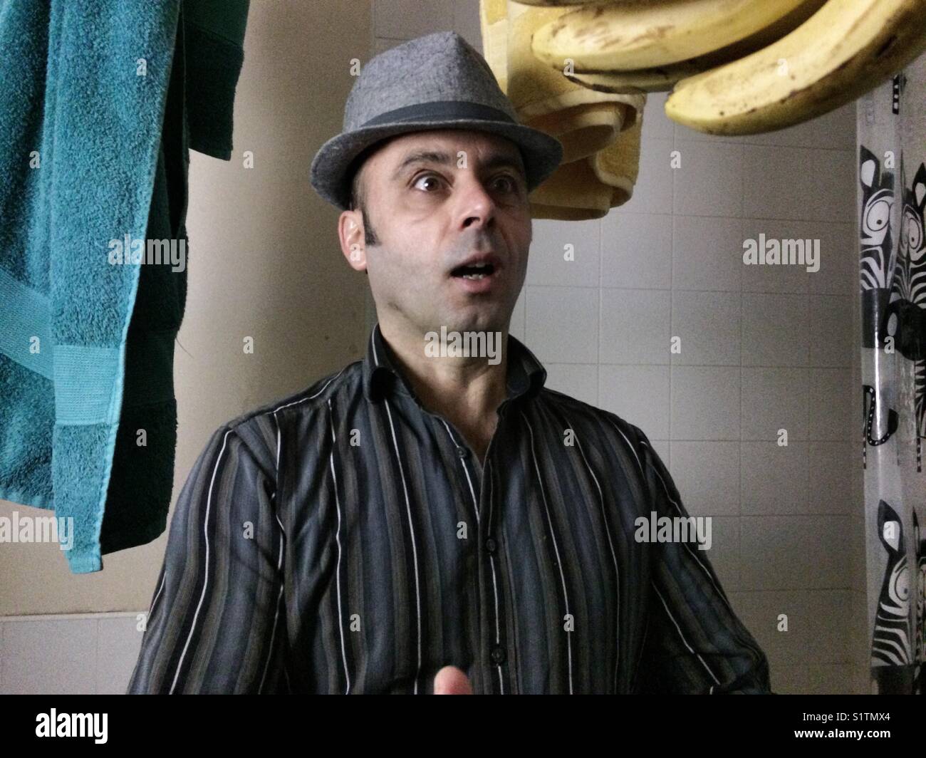 Porträt eines Mannes mit Hut ihre Überraschung mit gelben Bananen in der Luft, im Badezimmer Umgebung - Smartphone-aufgenommenes Stockfoto