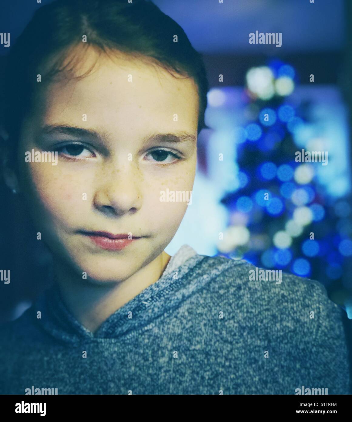 Portrait eines Mädchens mit natürlichen Ausdruck und Weihnachten Baum mit blauen Lichtern im Hintergrund leuchtet Stockfoto