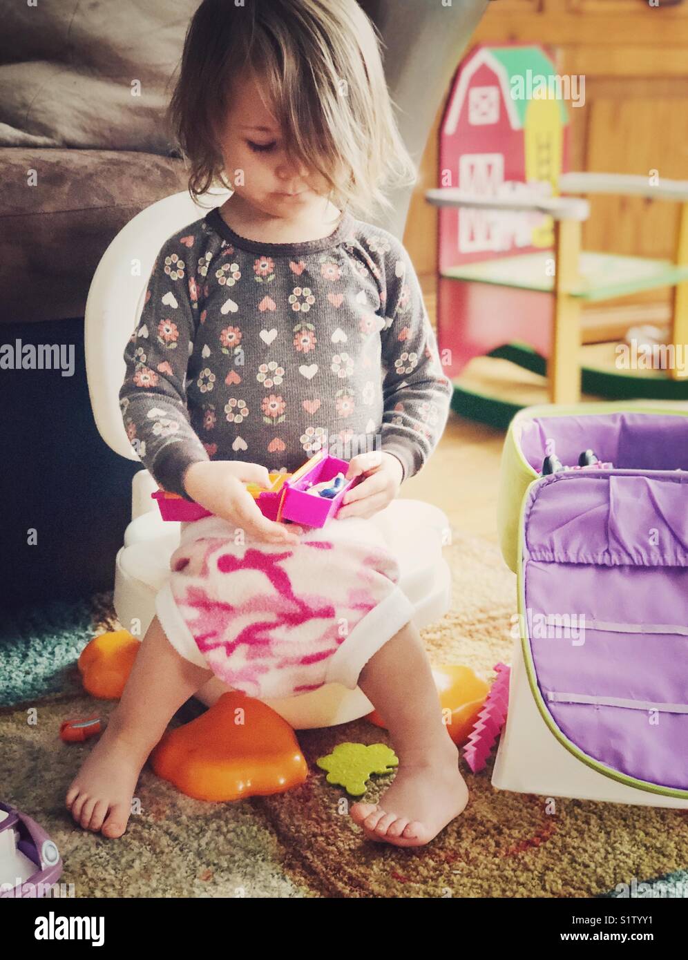 2 Jahre altes Kleinkind Mädchen sitzen auf potty Chair mit Spielzeug spielen, während wc Training Stockfoto