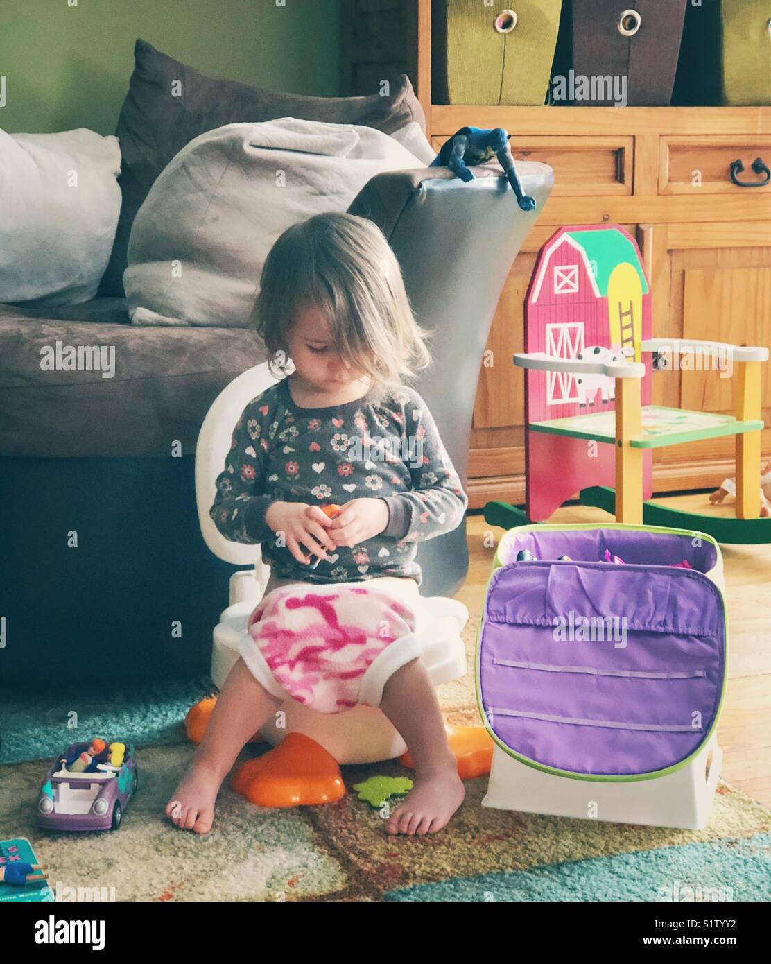Authentische, ehrliche lifestyle Bild von Kleinkind Mädchen sitzen auf potty Chair mit Spielzeug in Familienzimmer während wc Training Stockfoto