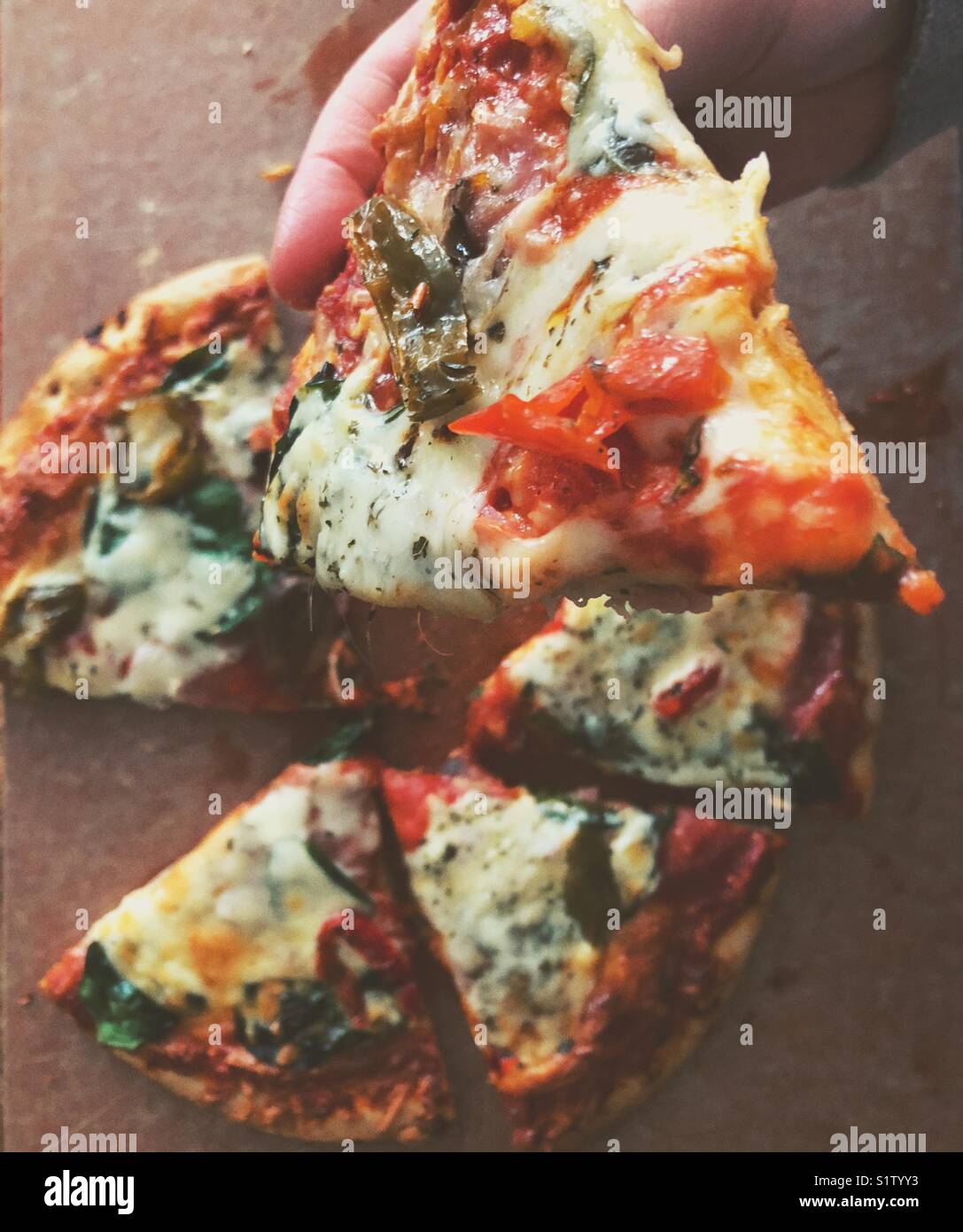 Essen ein Stück Pizza von Personen gesehen, die ist, um einen Bissen mit ganzen Pizza unten im Bild Hintergrund - Smartphone-aufgenommenes Stockfoto