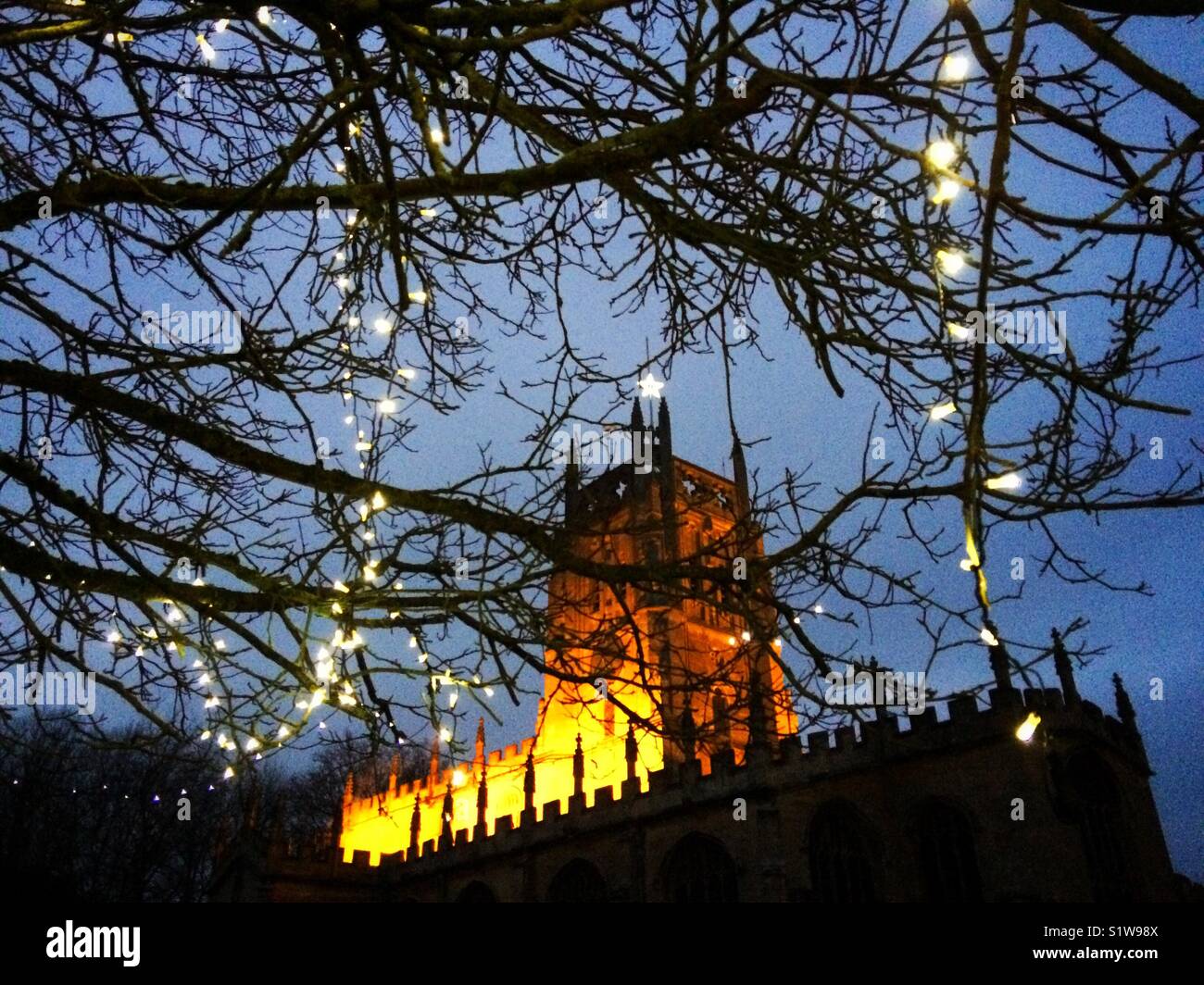 Flutlicht Cotswold Kirche mit Lichterketten an einem Baum auf dem Friedhof in Großbritannien Stockfoto