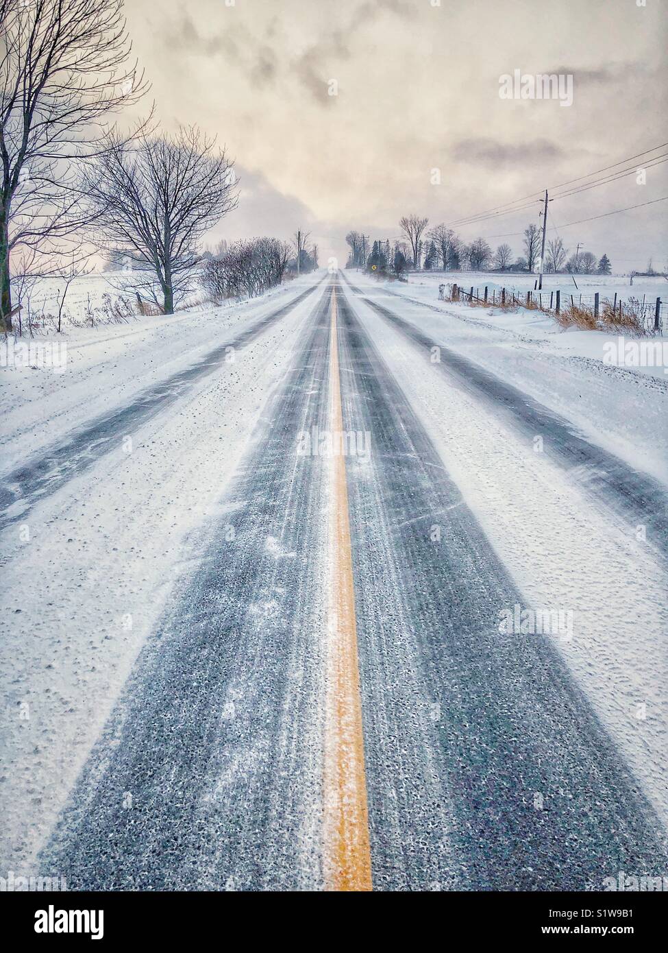 Schnee bedeckt leere Straße im ländlichen Ontario, Kanada mit Wind, Schnee wirbelt - Smartphone-aufgenommenes Stockfoto