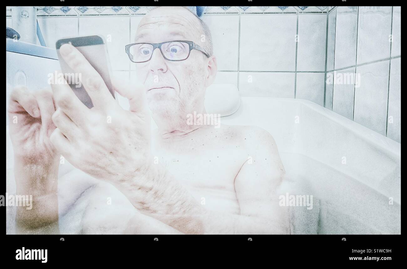 Im mittleren Alter Mann mit überrascht, schockiert Gesichtsausdruck in der Badewanne Blick auf Smartphone - Smartphone-aufgenommenes Stockfoto