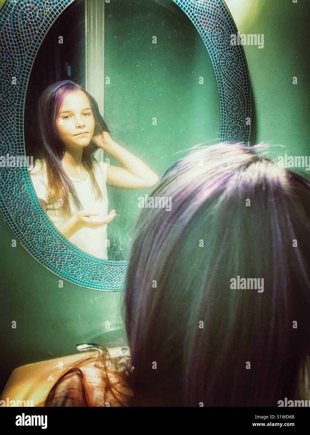 10 Jahre alte Mädchen mit lila Streifen in Haar an der Reflexion im Badezimmer spiegel Stockfoto